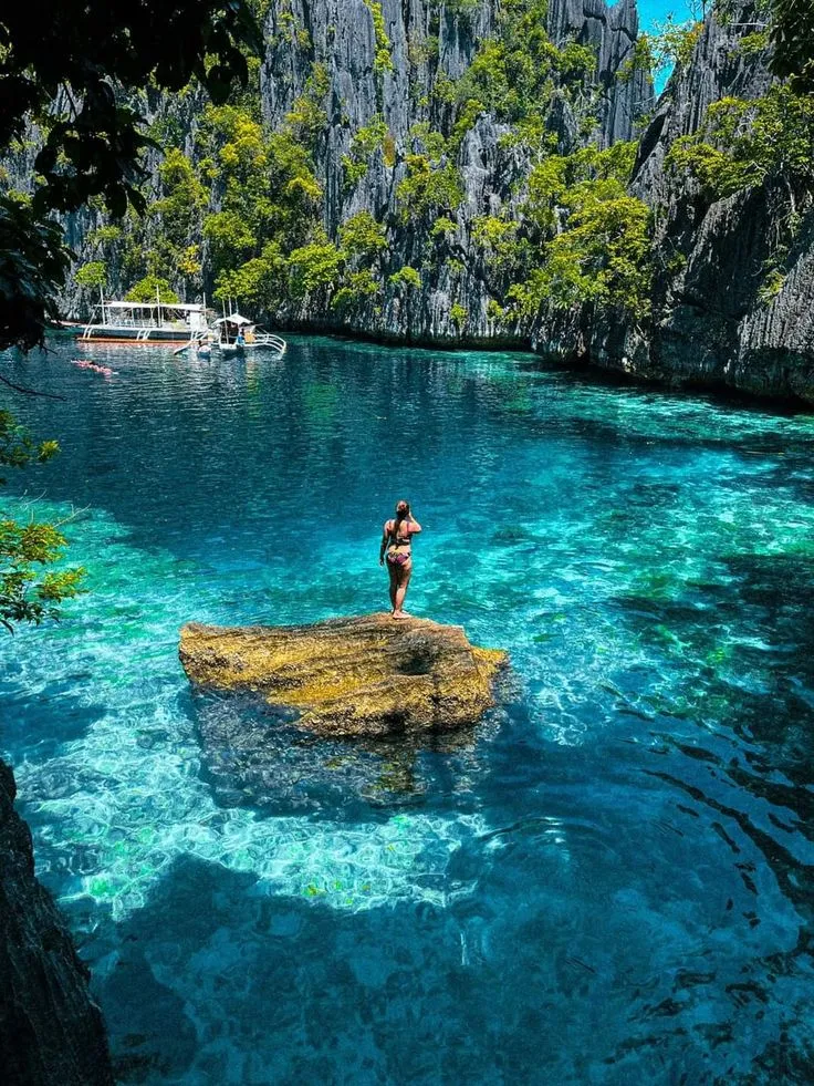 A swimmer standing on a rock in a turquoise lagoon in Coron, Palawan