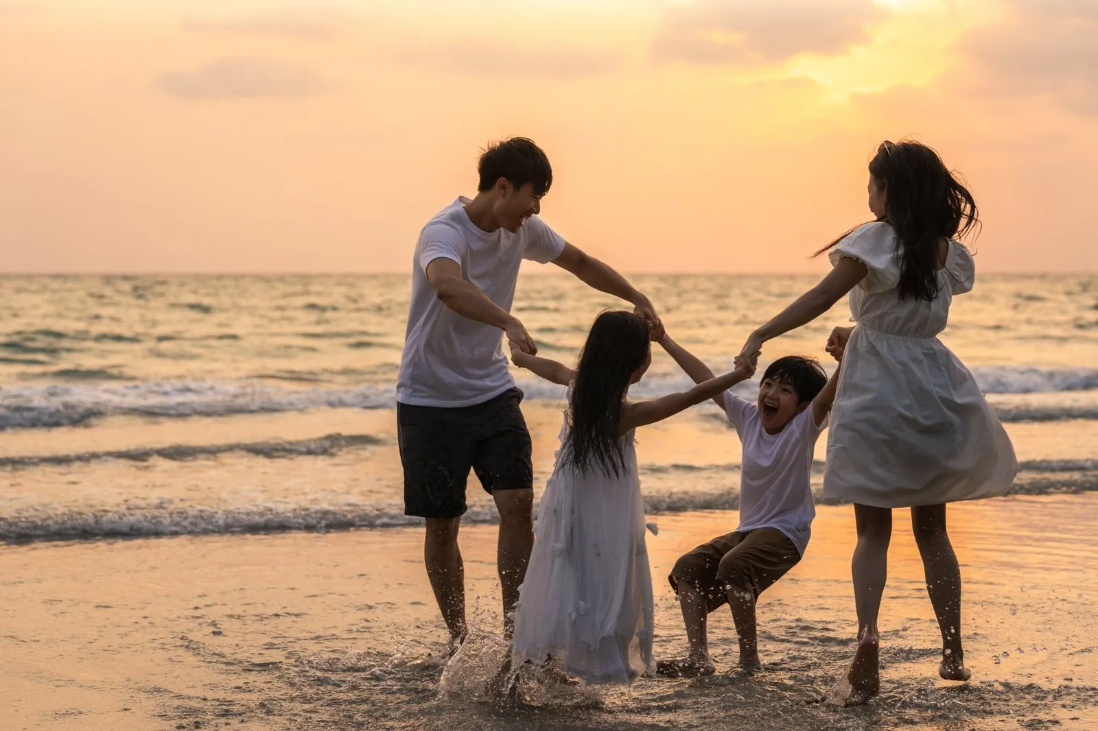 A family holding hands and playing in the surf at sunset
