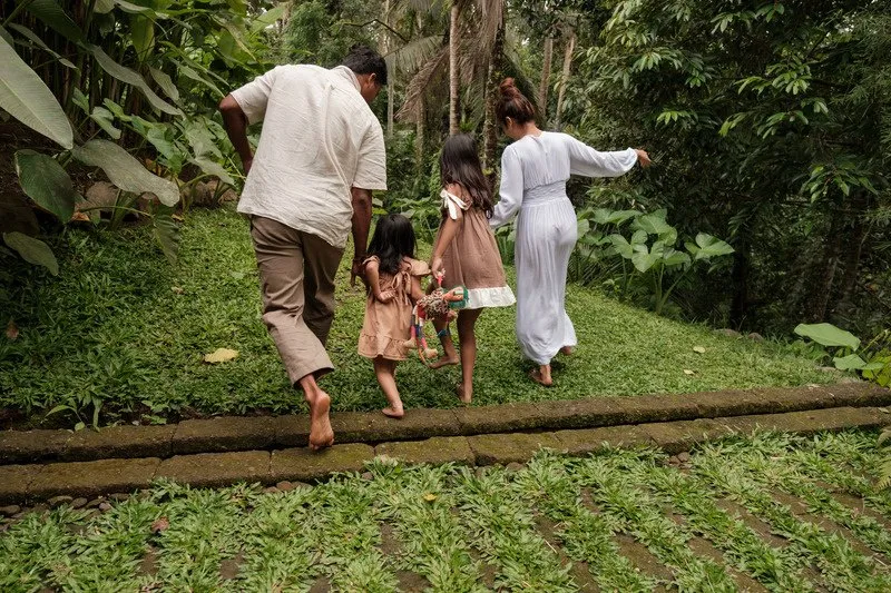 A family walking hand in hand along a leafy garden path