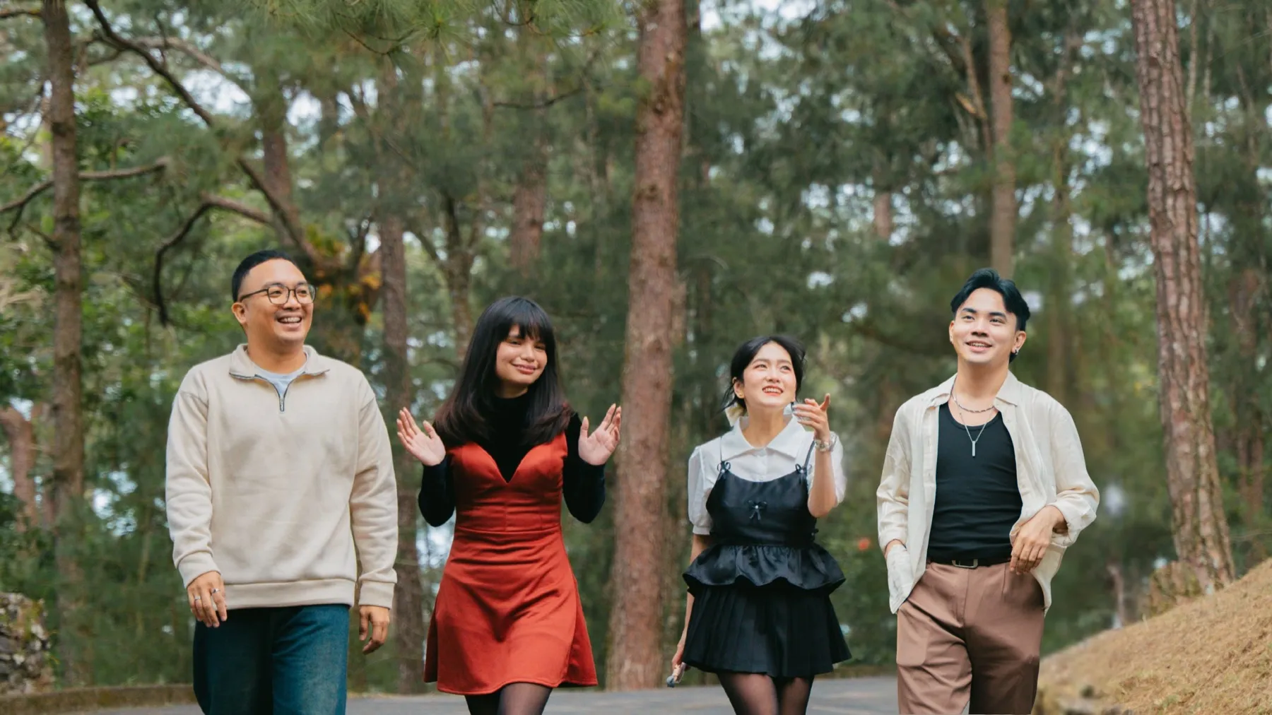 Four friends laughing as they walk together beneath tall pine trees