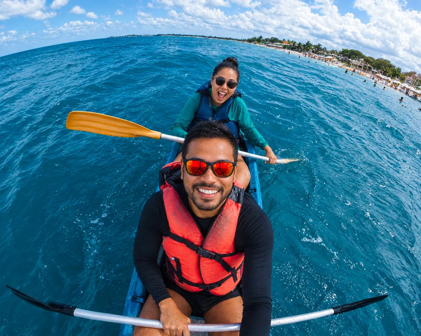 A smiling couple paddling a kayak on clear blue water