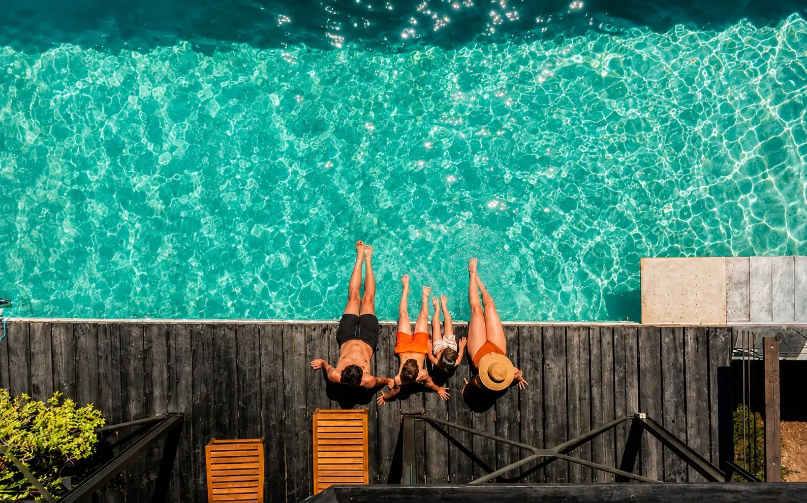 A family lying on a poolside deck, seen from above